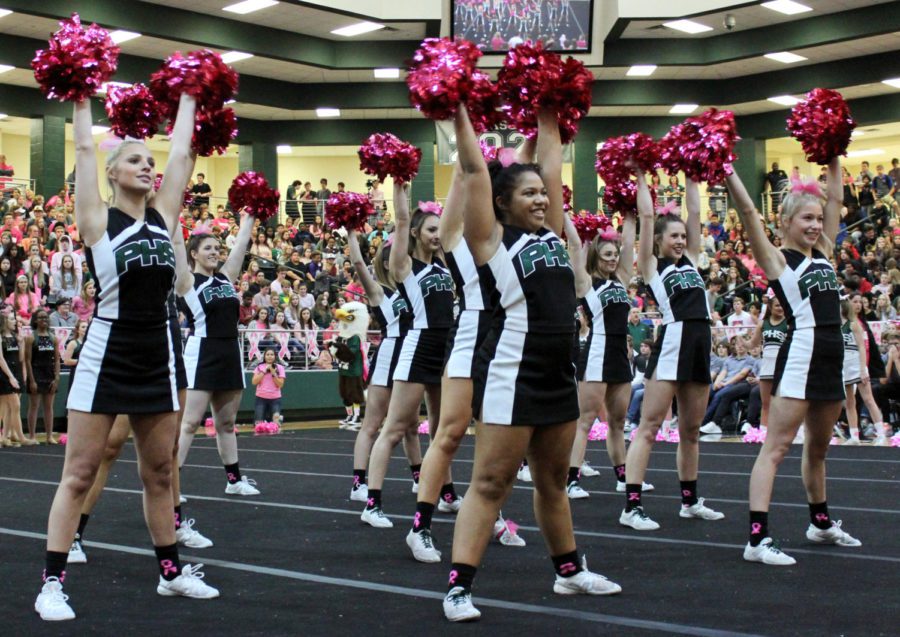 Varsity cheerleaders hold up their pink pom-poms during a cheer.  Senior Shae Ripple stands front and center in this shot. The cheerleaders coordinated with several groups to arrange the events of this pep rally. 