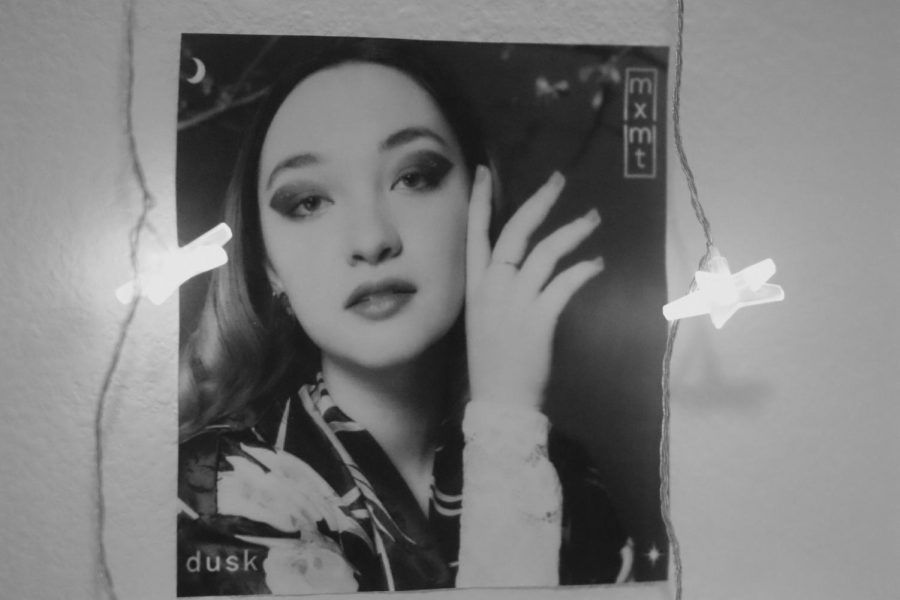 A black and white photo of Maia, otherwise known as mxmtoon, stands illuminated against a wall.  Throughout the album, Maia beautifully addresses beginning and ending a relationship, writer Rusty Joe Gonzales said. Her latest work is worth the listen. Plus, it tells a great story — even a few stories — in seven songs.