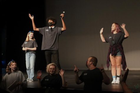 Arms raised in the air, senior Alex Oshunkentan leads everyone in a group warm up prior to the social starting. This is Oshunkentans second year in the department, snf he is the leader of the Procyon house. The social was held  Aug. 26 in the auditorium.
