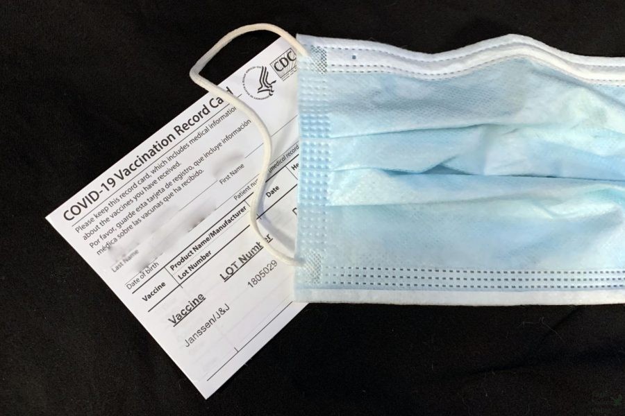 A teachers vaccine card sits with a disposable mask. This year, masks are optional for students. As of now, there is no virtual option for high school students.