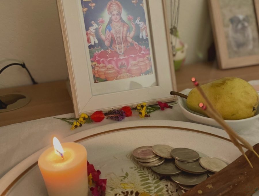 Due to COVID-19, a few large Diwali festivals were canceled this year. Kalyani Rao, the author of this article, ended up celebrating Diwali inside her house. She created this small portable altar for Lakshmi puja, using a tea light, varieties of garden flowers, a pear and grains of basmati rice as prashadam, aka an offering, for the goddess Lakshmi. The gathering also includes incense sticks and coins. A picture of Lakshmi sitting on her lotus flower rests in front of the offering plate, decorated with flowers at the base.