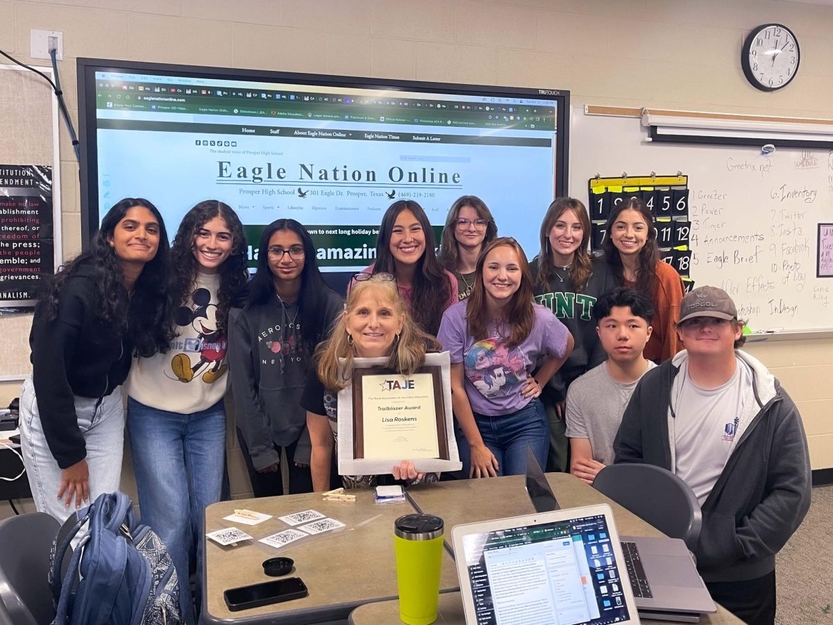 Standing in front of the board in the PHS news room, adviser Lisa Roskens holds up her TJAE Trailblazer Award. The 2023-2024 ENO staff surrounds her to celebrate the accomplishment. The photo features Anisha Mandem, Erica Deutsch, Srihitha Madepalli, Kaya Miller, Tess Gagliano, Lauren Clayton, Gracie Archibeque, Riley McConnell, Justin Wang, and Will Ligon