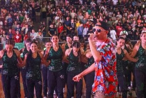 In front of the Talonettes, Principal Nick Jones speaks to the audience through a microphone. PHS hosted an aloha-themed pep rally Friday at 11:49 a.m. in the Arena. The varsity football team will play against Westlake at 7 p.m. on Thursday.