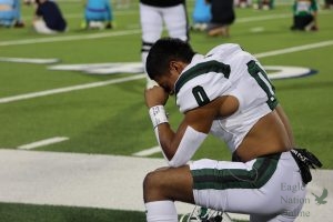 Kneeled to the ground, senior Leo Anguiano prays on the sideline before the first quarter starts. He earned the title "Offensive MVP" for this game, along with several others. The game was broadcast on WFAA channel 8.