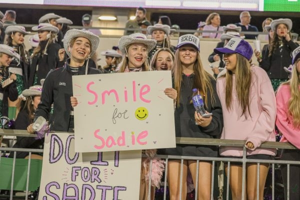 Holding up a 'Smile for Sadie' sign, senior Gavin Teague and junior Alyssa Milner stand in the Talonette section. The Talonettes performed a dance dedicated to their teammate Sadie Neddo. A prayer was held at the end of the game to honor her. 