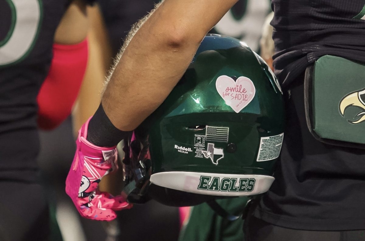 Helmet in hand, junior Cade Smallwood stands for the national anthem. The team displayed 'Smile for Sadie' stickers on their helmets to honor Talonette, Sadie Neddo. The students dressed up in pink and purple to show support, and honor her memory. 