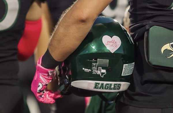 Helmet in hand, junior Cade Smallwood stands for the national anthem. The team displayed "Smile for Sadie" stickers on their helmets to honor Talonette junior Sadie Neddo after her death Oct. 14. The students dressed up in pink and purple to show support and honor her memory. 