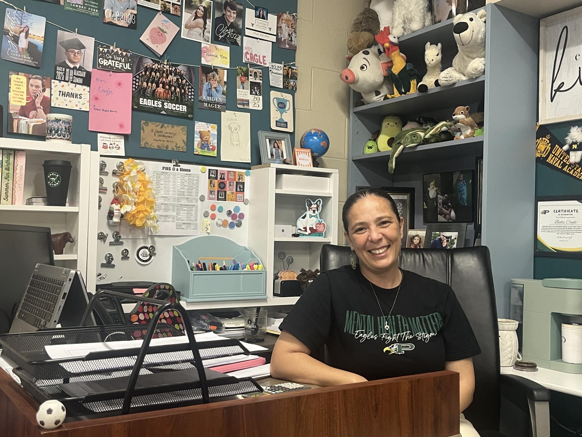 At her desk, AP Precalculus teacher Bediz Efeciner Cagle sits among some of the items in her classroom. Cagle decorates her room to make her students feel comfortable as they learn, hanging up their art pieces and providing stuffed animals for them. "Some people go and get a one (during a test), like a emotionally supportive stuffed animal, right?" Cagle said. "So that's the reasoning behind it, why I have all those toys and during the years."