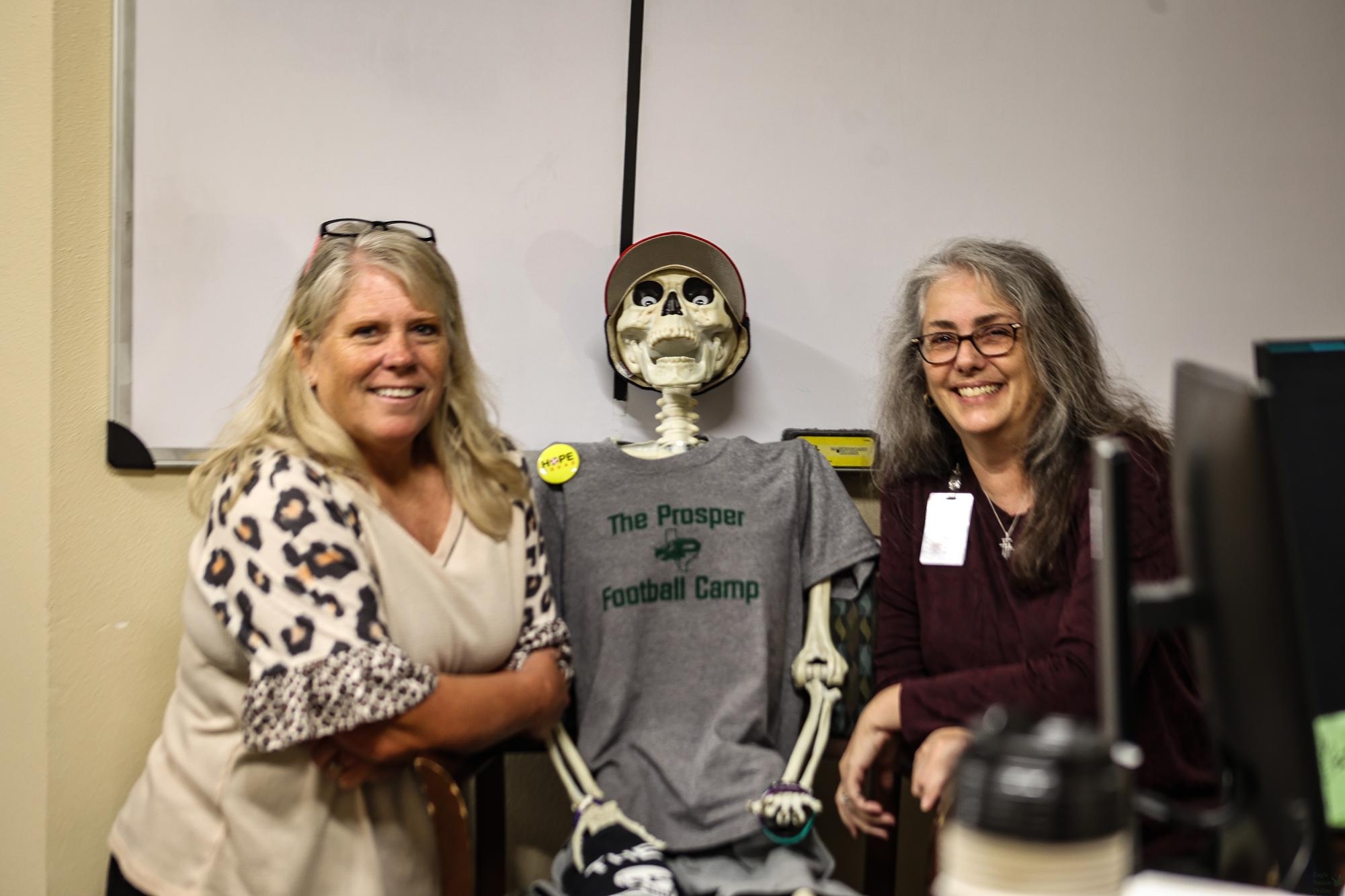 Smiling at the camera, secretaries Renee O'Brien and Melinda Hoover sit with Bones the Skeleton. The two brought Bones to PHS in the Halloween in 2023. “People joke about, ‘Oh, if you stay here that long, well, this is what you’re going to look like,” O’Brien said. “This is my 14th year in Prosper. I was at Rogers for ten, and this is my fourth year here at PHS."